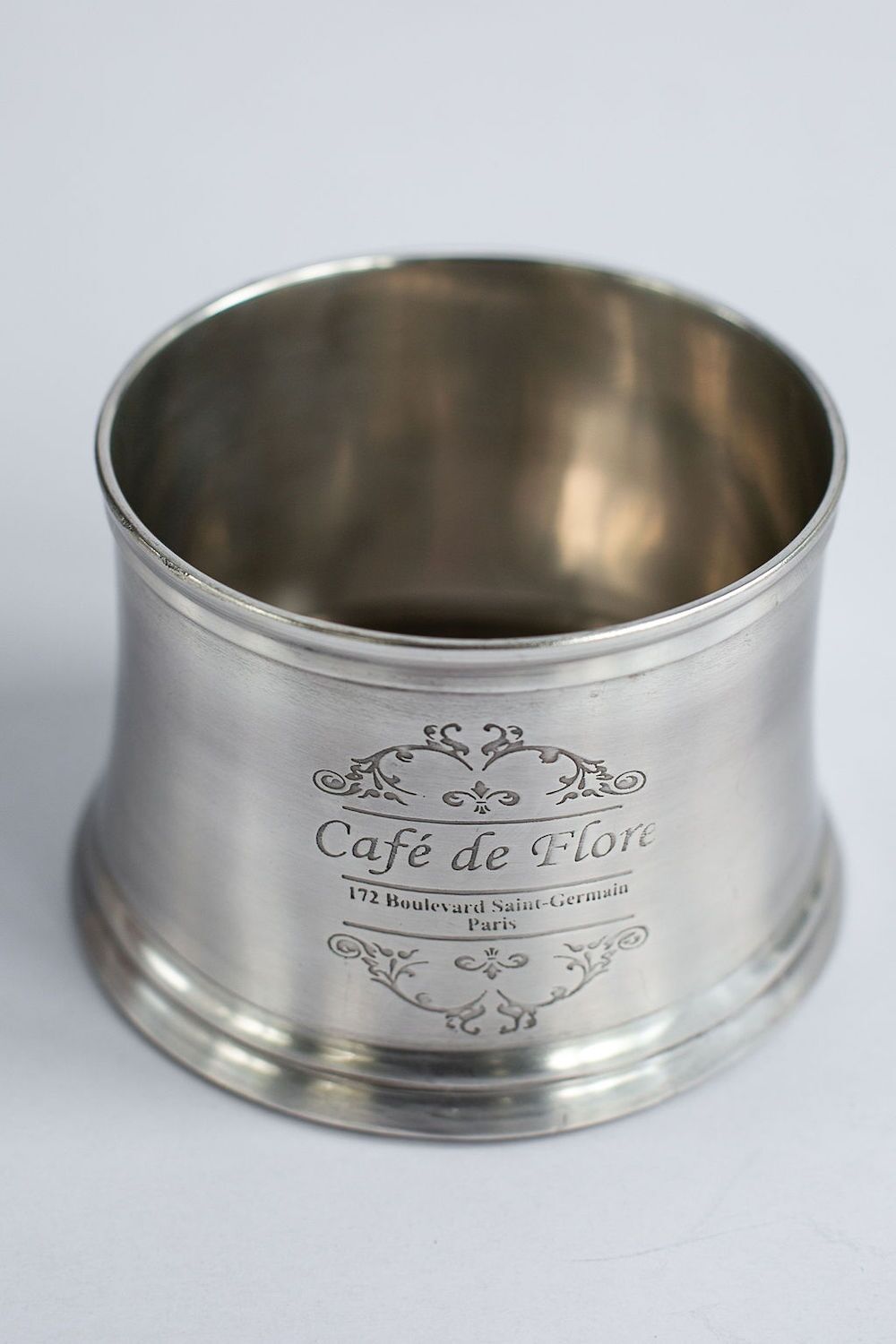 Polished silver cup with ornate engraving saying 'Café de Flore' and address in Paris (172 Boulevard Saint-Germain).