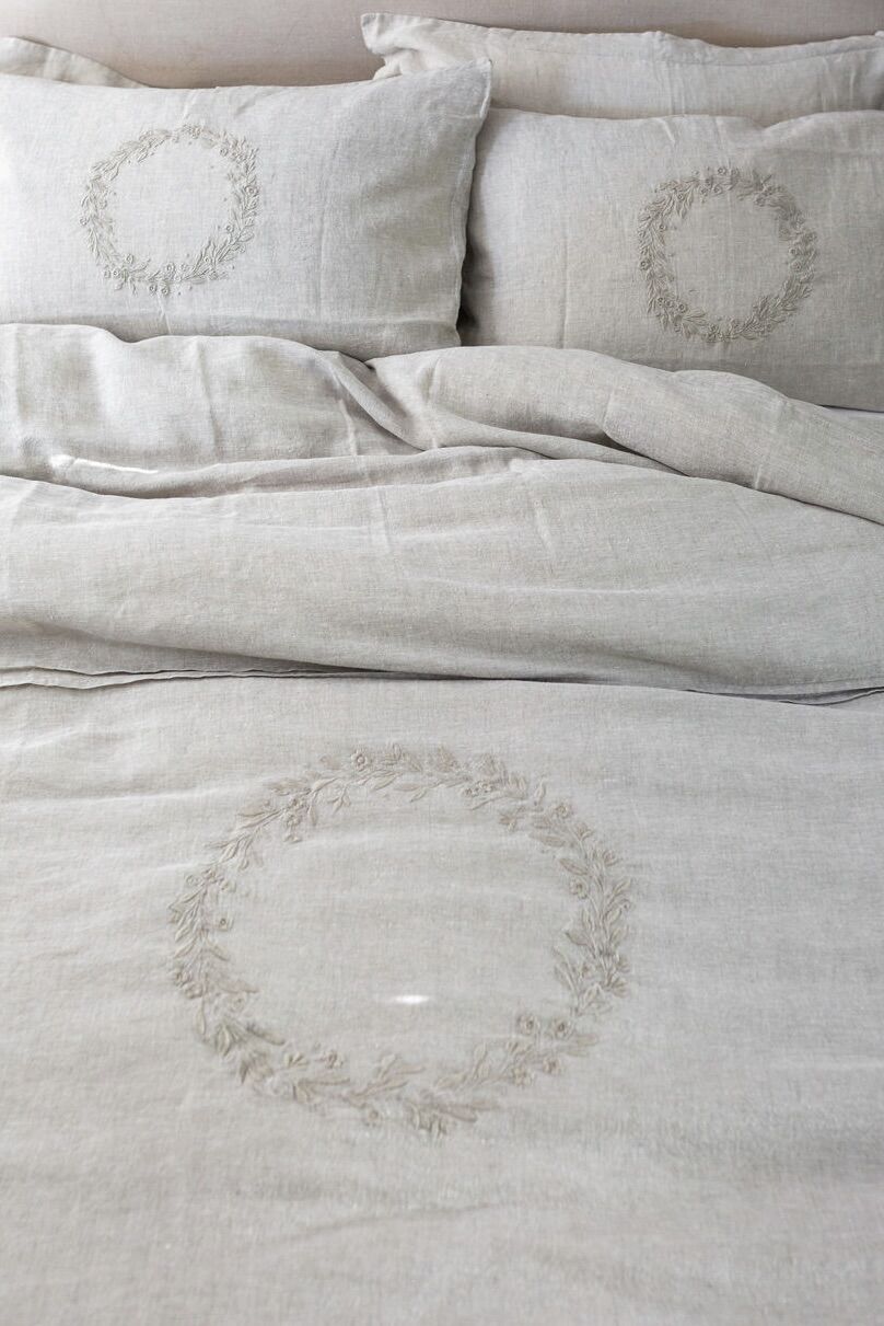 Light gray linen bedding with embroidered circular wreaths on duvet and pillows.
