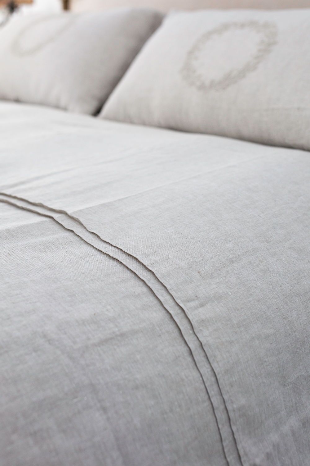 Close-up of light gray linen fabric with a visible seam, likely on a sofa or bed upholstery.