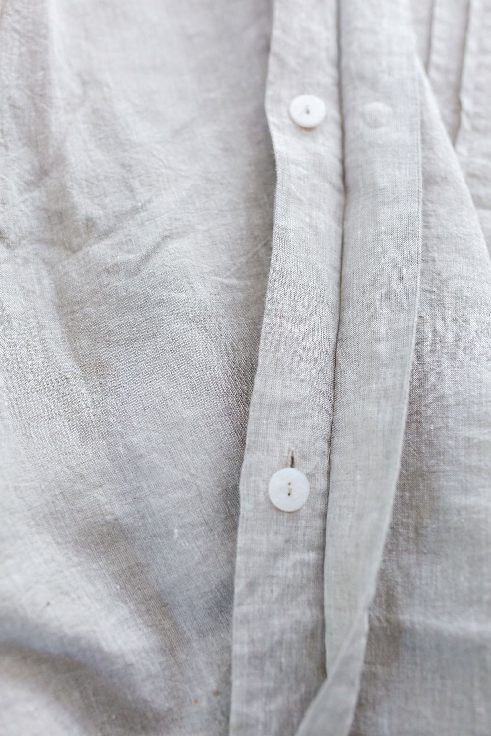 Close-up of a light gray linen shirt with white buttons along the placket showing the fabric texture.