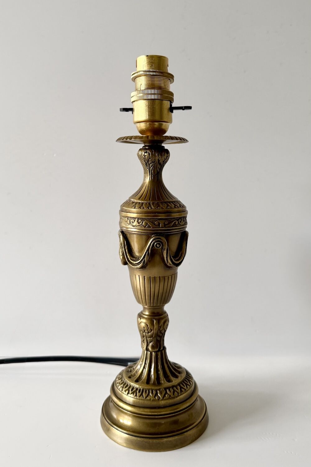 Ornate brass lamp base with decorative engravings and a bare bulb socket on top.