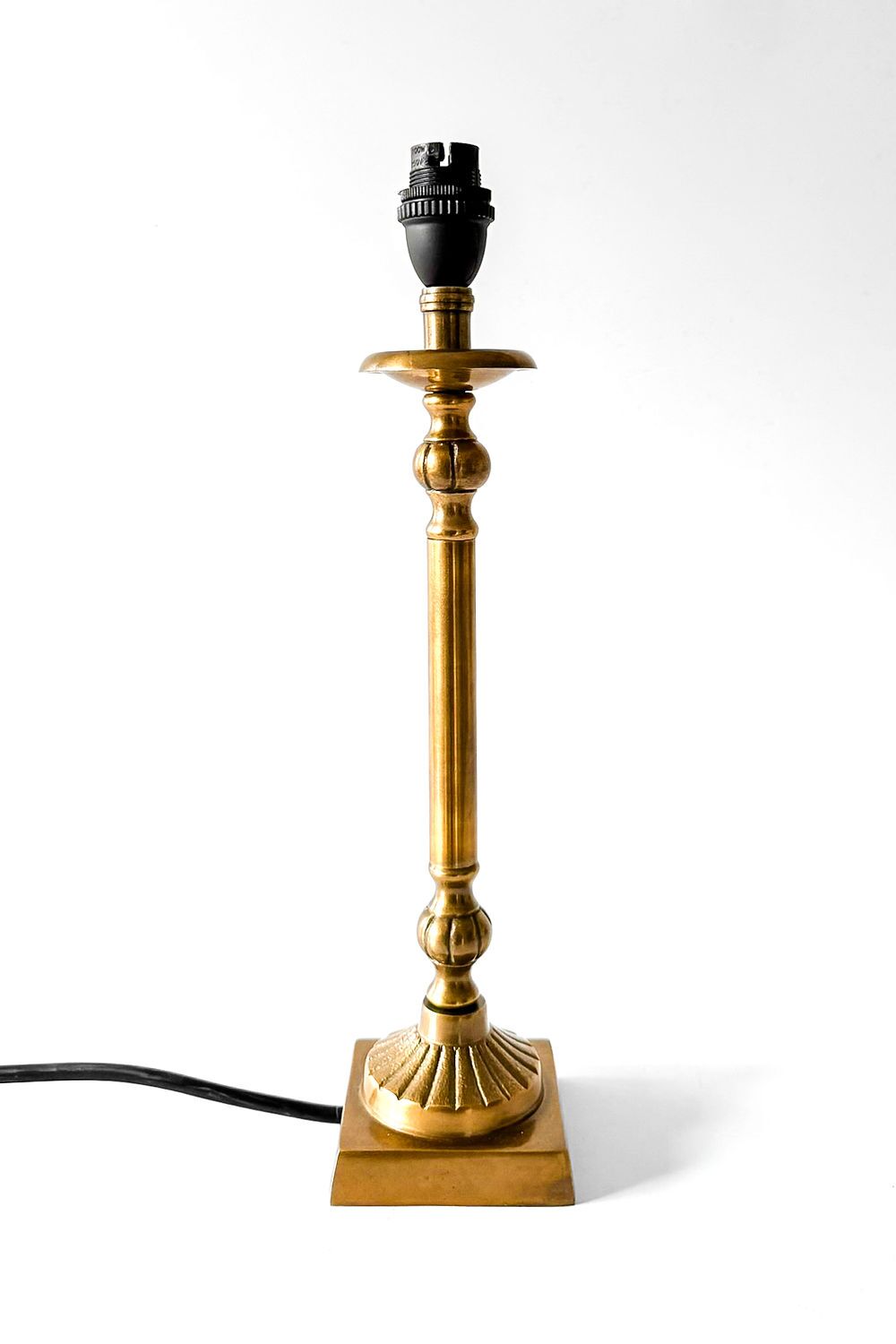 Tall brass table lamp with ornate turned stem and square base, cord trailing to the left (no lampshade).