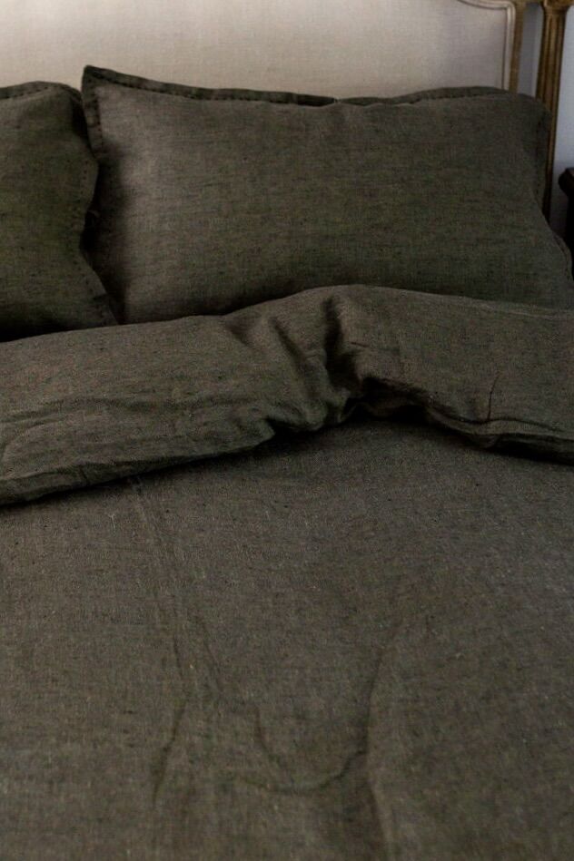 Dark gray bed with wrinkled blanket and two matching pillows against a headboard in a cozy bedroom.