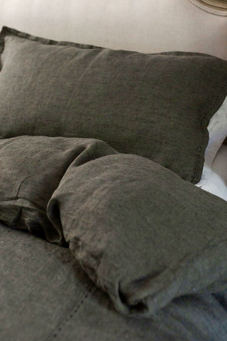 Close-up of a dark gray pillow and blanket on a bed, with soft fabric and stitching visible.