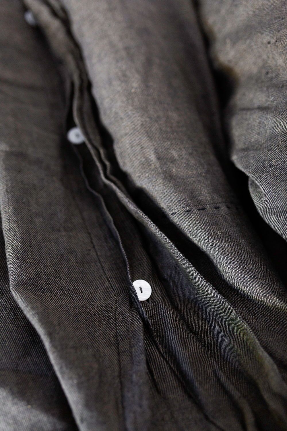 Close-up of dark gray fabric with white buttons along a shirt placket, showing texture and folds.