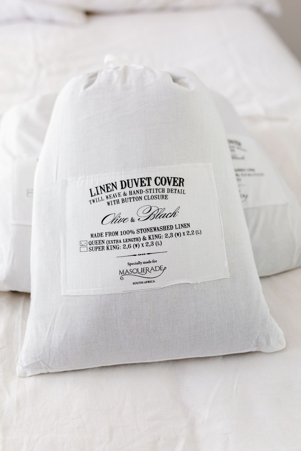 White linen duvet cover in packaging with a printed label showing sizes (Queen and Super King) and Masquerade branding.