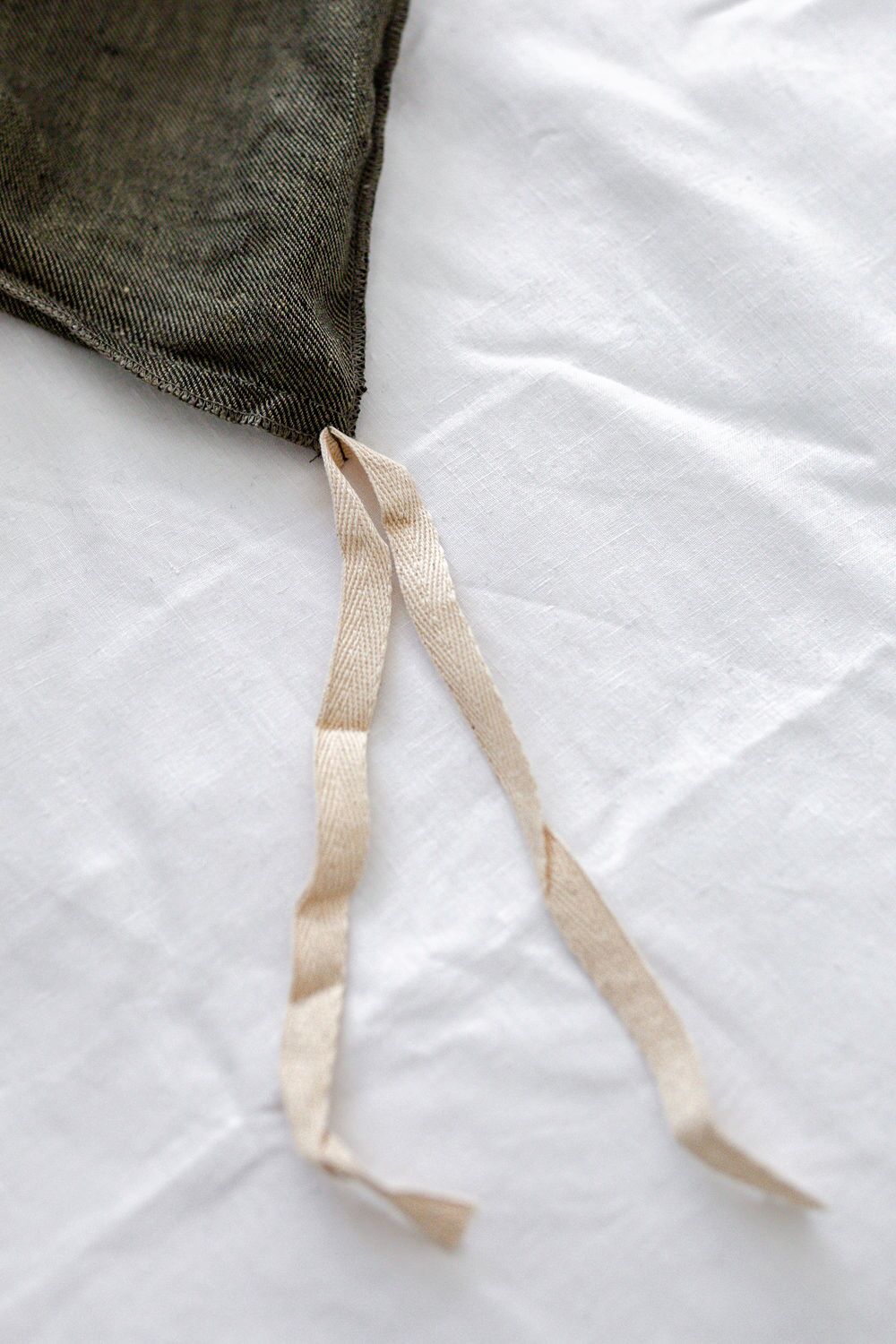 Close-up of a beige fabric drawstring emerging from the corner of a dark bag on a white background.