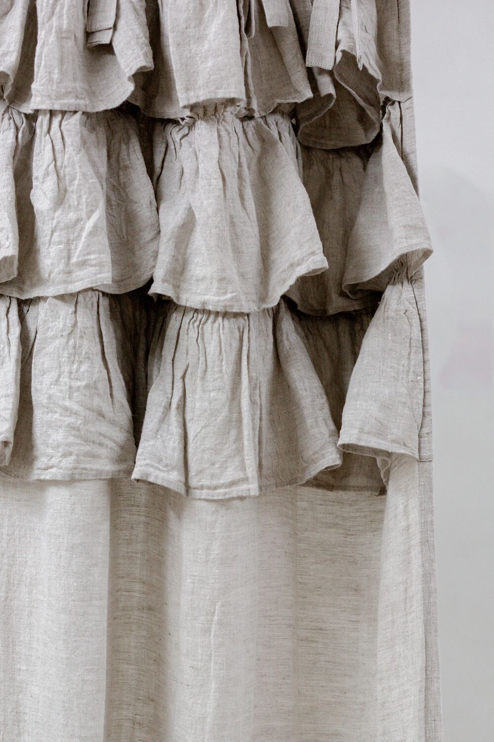 Close-up of beige linen fabric with multiple gathered ruffles on a garment edge.