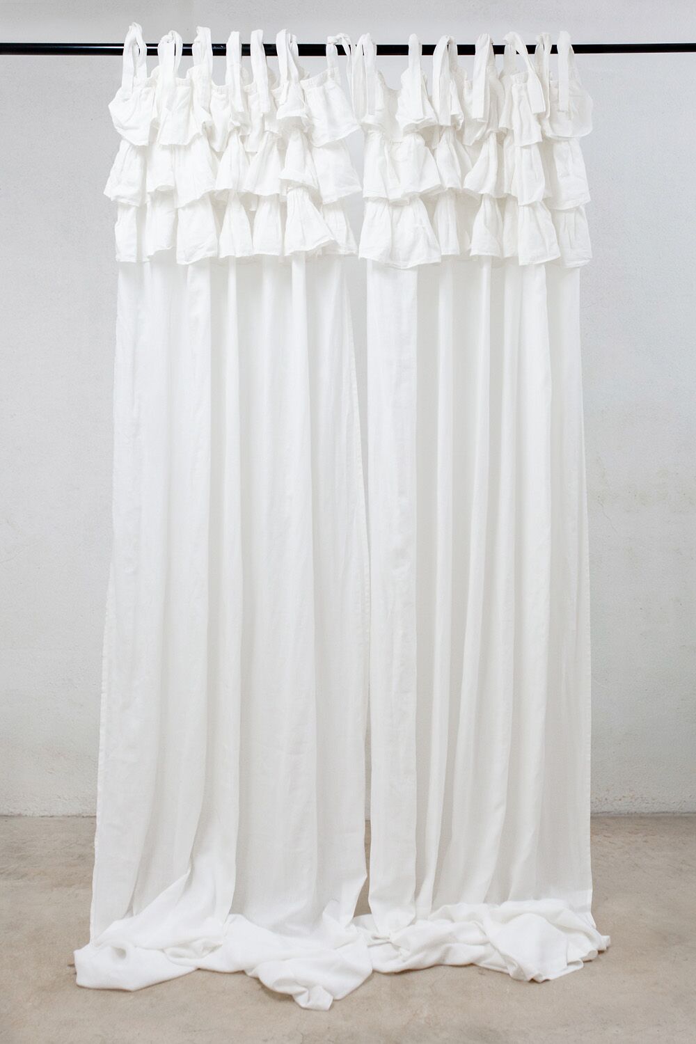 White curtains with layered ruffles hanging from a black rod, pooling on the floor.