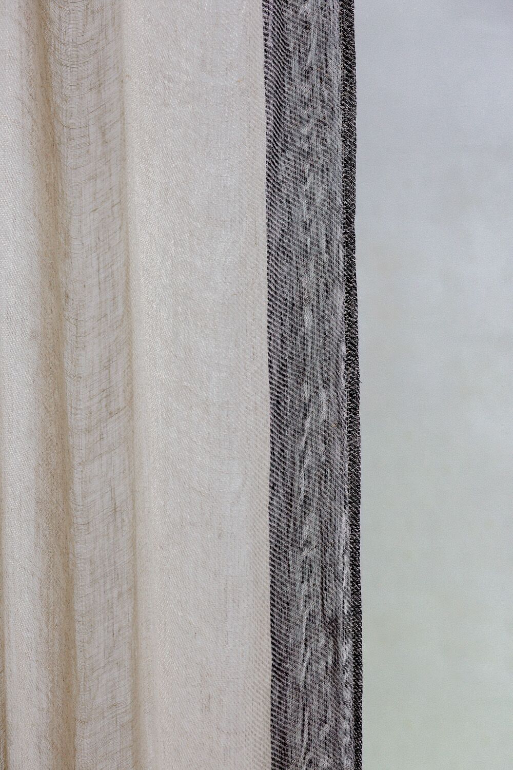 Close-up of a beige sheer curtain with a darker sheer panel on the right, against a pale window background.