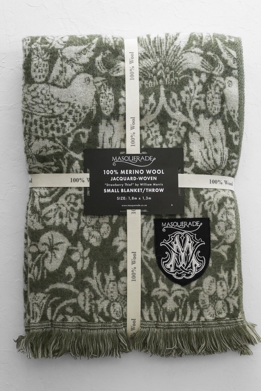 Jacquard-woven green and beige merino wool throw with fringed ends, Masquerade label and crest patch